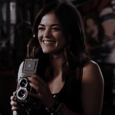 a woman holding an old fashioned camera in her right hand and smiling at the camera