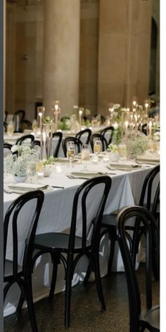 a long table is set with black chairs and white linens for an elegant dinner