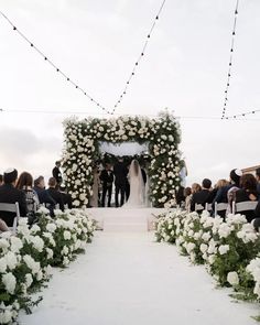 an outdoor ceremony with white flowers and greenery on the aisle, surrounded by string lights