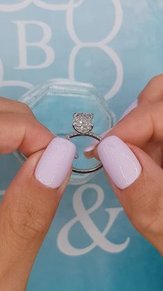 a woman's hands holding a ring with a diamond on it and a pink manicure