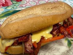 a sandwich with meat, cheese and peppers on it sitting on a floral table cloth