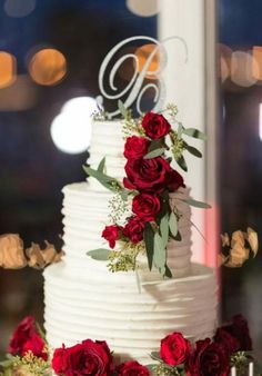 a white wedding cake with red roses and greenery