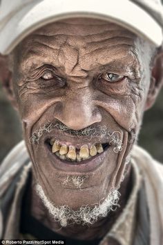 an old man with white hair and beard wearing a baseball cap smiles at the camera