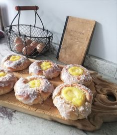 a wooden cutting board topped with donuts covered in icing and powdered sugar