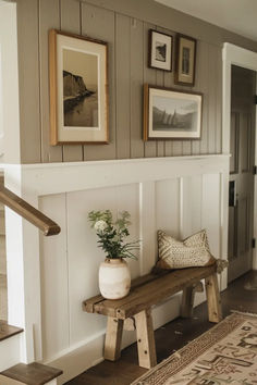 a wooden bench sitting in front of a wall with pictures on it and a potted plant