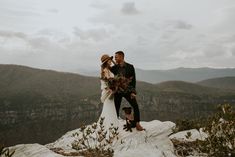 a bride and groom standing on top of a mountain