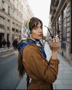 a woman is standing on the street holding something in her hand and looking off to the side