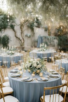 a table set up with blue linens and white flowers, gold chargers and candles