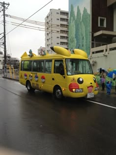 a yellow bus with surfboards on top drives down the street in front of people