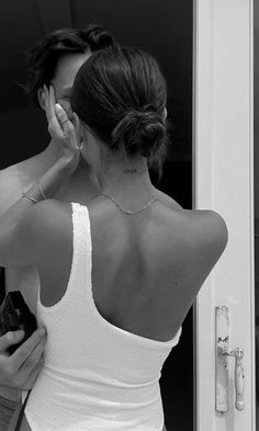 a woman in a white tank top is looking at her cell phone while standing by a door