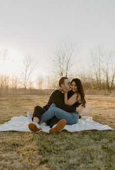 a man and woman sitting on top of a blanket in the middle of a field