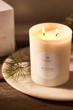 a white candle sitting on top of a table next to a box and some pine branches