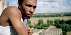 a man with no shirt on leaning against a wall looking down at the ground below