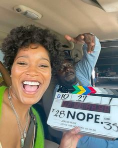 a woman holding up a clapper in the back of a car with another man behind her