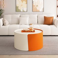 an orange and white coffee table in a living room with two paintings on the wall