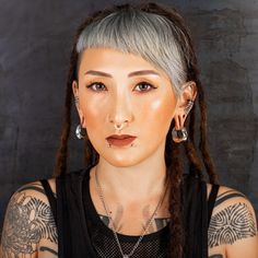 a woman with grey hair and piercings on her ears is looking at the camera