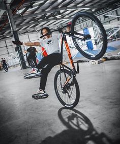 a man doing tricks on his bike in an indoor area with other people around him