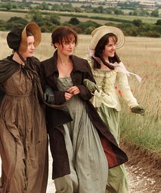 three women walking down a dirt road in long dresses and hats, one wearing a hat