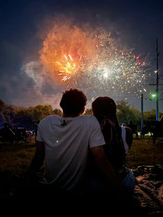 two people sitting on the ground watching fireworks