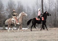 two people are riding horses in the snow near some trees and bushes, while another person is on horseback behind them