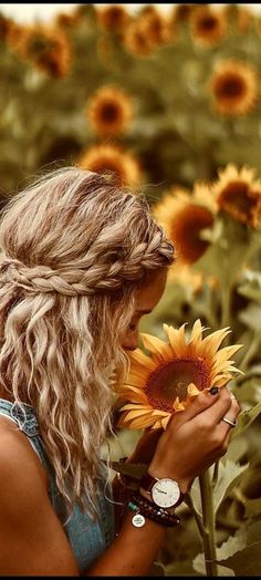 a woman standing in a field of sunflowers with her hands on the flower