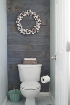 a white toilet sitting in a bathroom next to a wooden wall with a wreath on it