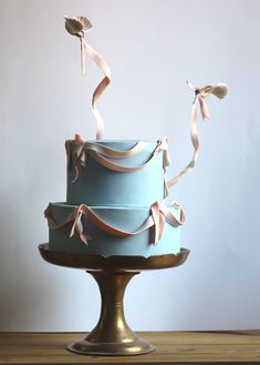 a three layer blue cake with ribbons on it's sides and two birds flying over the top