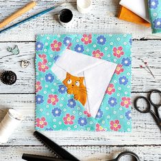 scissors, thread, and sewing supplies on a white wooden table with an orange cat in the envelope