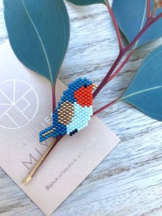 a needled bird brooch sitting on top of a piece of paper next to a plant