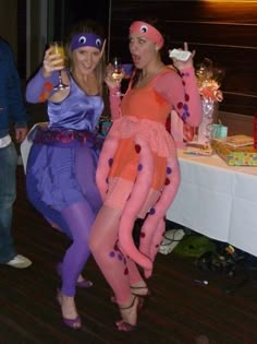 two women dressed in costumes pose for the camera while holding wine glasses at a party