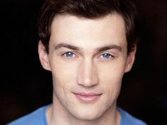 a close up of a person wearing a blue shirt and smiling at the camera with his eyes wide open