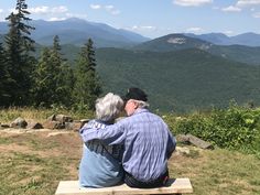 an older couple sitting on a bench looking at the mountains in the distance with their backs to each other