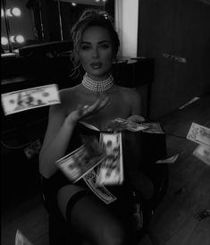 a woman is sitting in a chair holding magazines and looking at the camera while wearing pearls