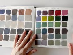 two hands are holding an open book with many different color swatches on the pages