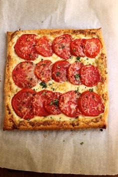 a square pizza topped with tomatoes and cheese on a piece of wax paper covered in grease