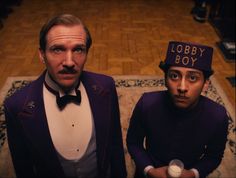 two men in tuxedos are sitting on a rug and one is looking at the camera