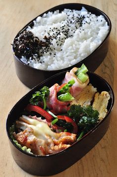 two black containers filled with rice, meat and veggies on top of a wooden table