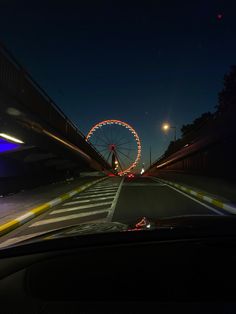 a ferris wheel is lit up at night in the distance as cars drive down the road