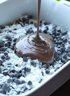 a chocolate sauce being poured into a bowl filled with white rice and blueberries on the side