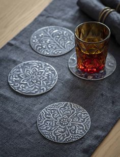 three glass coasters sitting on top of a table next to a cup and napkin