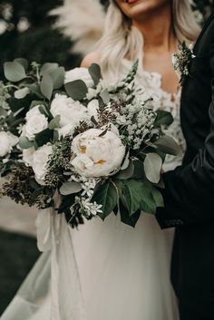 a bride holding a bouquet of white flowers and greenery