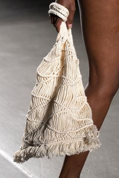 a close up of a person's legs holding a white bag with fringes on it