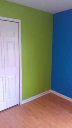 an empty room with blue and green walls, hard wood flooring and white doors