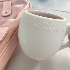 a hand holding a white coffee cup next to a pink purse on a counter top