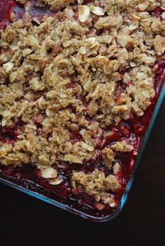 a close up of a dessert in a glass dish on a table with fruit and crumbs