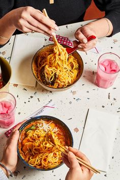 two people eating noodles with chopsticks at a table