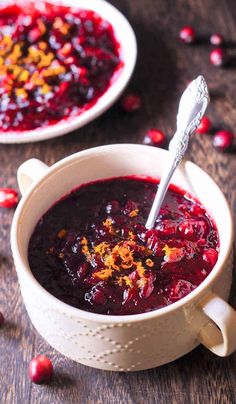 two white bowls filled with cranberry sauce on top of a wooden table next to a spoon