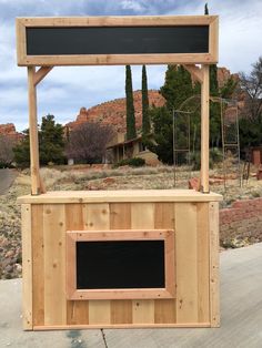 a wooden stand with a chalkboard on it in the middle of a road next to some trees