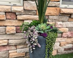 a tall planter filled with succulents and other plants next to a brick wall