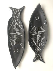 two black fish shaped sculptures sitting on top of a white wall next to each other